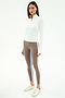A woman wears the SPLITS59 Tess Rigor Half Zip Waist Length top in white, taupe leggings with blue and brown side stripes, and white sneakers, standing against a plain white background.