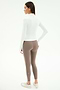 A woman stands facing away, wearing the SPLITS59 Tess Rigor Half Zip Waist Length top in white, taupe nylon spandex leggings with a white side stripe, and white sneakers against a plain background.