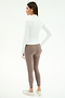 A woman stands facing away, wearing the SPLITS59 Tess Rigor Half Zip Waist Length top in white, taupe nylon spandex leggings with a white side stripe, and white sneakers against a plain background.