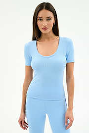 A woman faces forward against a white background, wearing the SPLITS59 Ashby Rib Short Sleeve in Skylight, a light blue top with short sleeves and scoop neck, paired with matching fitted pants made from a soft modal spandex blend.