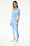 A woman wears the SPLITS59 Ashby Rib Short Sleeve in Skylight and matching leggings with dark blue side stripes, both crafted from a soft modal-spandex blend, paired with white sneakers against a plain white background.