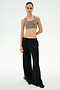 A person stands against a plain background, facing forward with a neutral expression, wearing the SPLITS59 Dallas French Terry Wide Leg Sweatpant in Black/Lentil—crafted from soft 100% cotton—which features loose black pants with side stripe detail and is paired with a taupe sports bra.