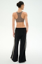 A person stands facing away against a plain white background, wearing a brown sports bra paired with the SPLITS59 Dallas French Terry Wide Leg Sweatpant in Black/Lentil, featuring side stripes and crafted from soft 100% cotton fabric.