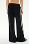 A person is shown from the back, wearing SPLITS59 Dallas French Terry Wide Leg Sweatpants in Black/Lentil—loose-fitting black pants with white side stripes made from soft cotton terry fabric—against a plain white background.
