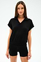 A woman wearing the SPLITS59 Evie Fleece Sleeveless Polo in black, paired with black shorts, stands against a plain light background. The look features sporty style and comfort.