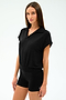 A woman with straight brown hair wears the SPLITS59 Evie Fleece Sleeveless Polo in black, paired with black fitted shorts, standing against a plain light background.