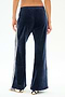 A person is shown from the back wearing SPLITS59's Heritage Velour Pant in Indigo/White, featuring white side stripes and white sneakers. The pants are made from a soft polyester blend, set against a plain white background.