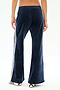 A person is shown from the back wearing SPLITS59's Heritage Velour Pant in Indigo/White, featuring white side stripes and white sneakers. The pants are made from a soft polyester blend, set against a plain white background.