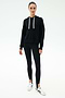 A person stands facing forward in a SPLITS59 Joey Fleece Hoodie in black, black spandex blend leggings with stirrups, and white sneakers against a plain white background.