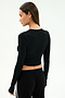 A woman with long brown hair faces away from the camera, wearing the SPLITS59 Louise Rib Long Sleeve Crop in black and black pants against a simple light background.