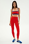 A woman stands against a plain background wearing the SPLITS59 Monah Rigor Bra in Lotus Red/Cobalt, paired with matching leggings and blue athletic shoes.