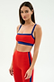 A woman wears the SPLITS59 Monah Rigor Bra in Lotus Red/Cobalt with matching high-waisted leggings, standing against a plain white background.