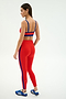 A woman in profile wears the SPLITS59 Monah Rigor Bra in Lotus Red/Cobalt with matching leggings and blue Adidas sneakers, set against a plain light background.