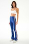Woman wears a spandex white crop top, SPLITS59 Raquel High Waist Supplex Flare - Cobalt/Creme pants, and white sneakers against a plain background.