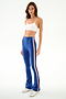 Woman wears a spandex white crop top, SPLITS59 Raquel High Waist Supplex Flare - Cobalt/Creme pants, and white sneakers against a plain background.