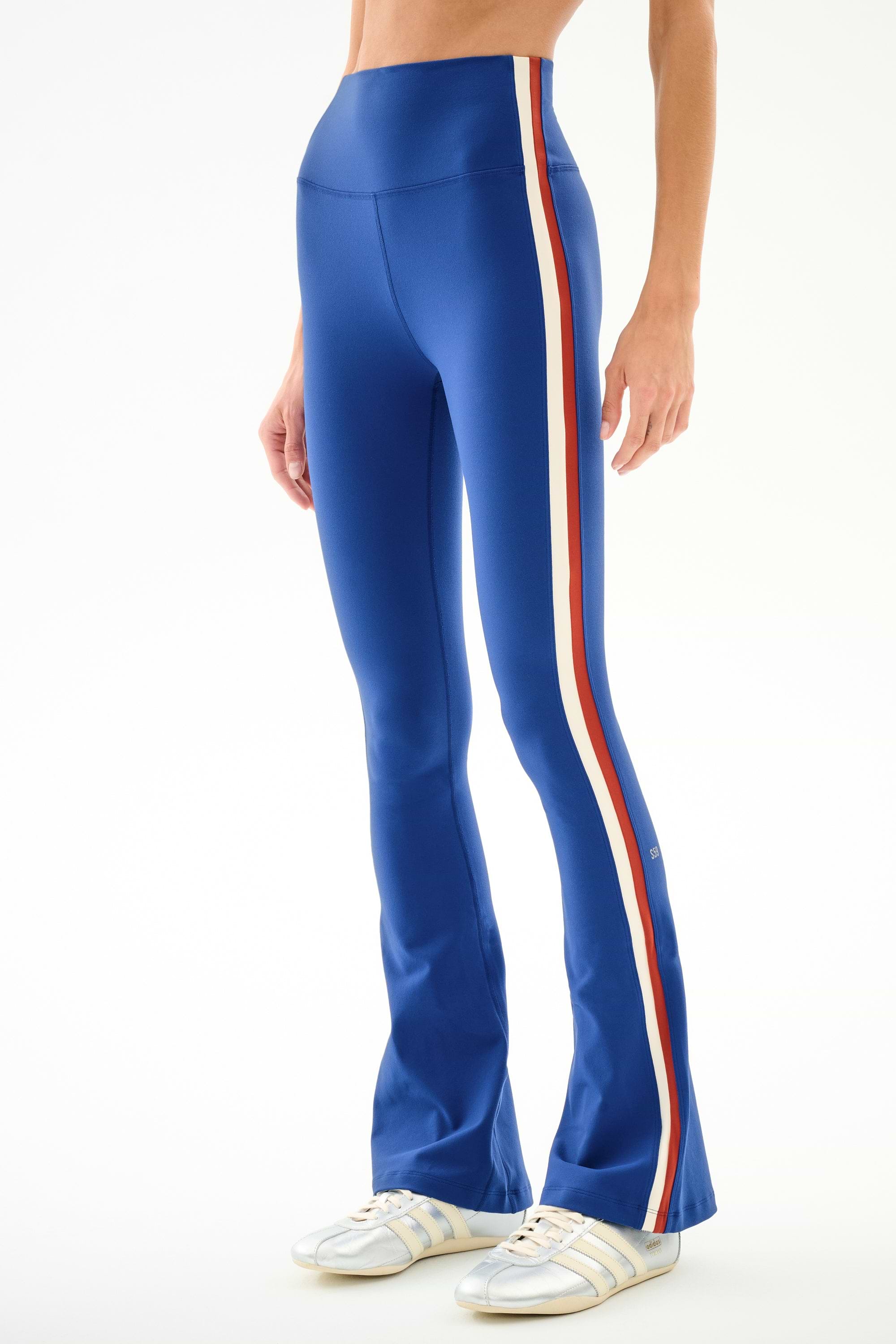 Model wearing SPLITS59 Raquel High Waist Supplex Flare - Cobalt/Creme with white sneakers, shown from mid-torso down against a plain background.