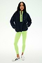 A woman stands facing forward against a plain white background, wearing the SPLITS59 Reese Sherpa Half Zip Pullover in Indigo/Limeade—crafted from 100% polyester and featuring neon green accents—paired with light green leggings and white sneakers with black details.