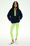 A woman stands facing forward against a plain white background, wearing the SPLITS59 Reese Sherpa Half Zip Pullover in Indigo/Limeade—crafted from 100% polyester and featuring neon green accents—paired with light green leggings and white sneakers with black details.