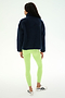 A woman stands with her back to the camera, wearing the SPLITS59 Reese Sherpa Half Zip Pullover in Indigo/Limeade, paired with neon green leggings and white sneakers against a plain light background.