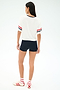 A person stands on a white background wearing the SPLITS59 Rex Varsity Jersey V-Neck in White/59, black shorts, white socks with red stripes, and white sneakers with red details.