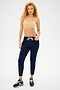 A person with curly hair wears the Loren Seamless Bra in Nude by Splits59 and navy joggers, standing with one hand in a pocket. The chafe-free fabric makes it ideal for gym workouts.