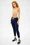 A person with curly hair stands in a neutral pose, wearing a Splits59 Loren Seamless Bra in nude and navy blue joggers made of chafe-free fabric, paired with sneakers, against a plain background.