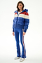 A woman wears the SPLITS59 Aspen Puffer Jacket - Cobalt/Creme with blue flared pants, side stripes, and silver sneakers against a plain white background.