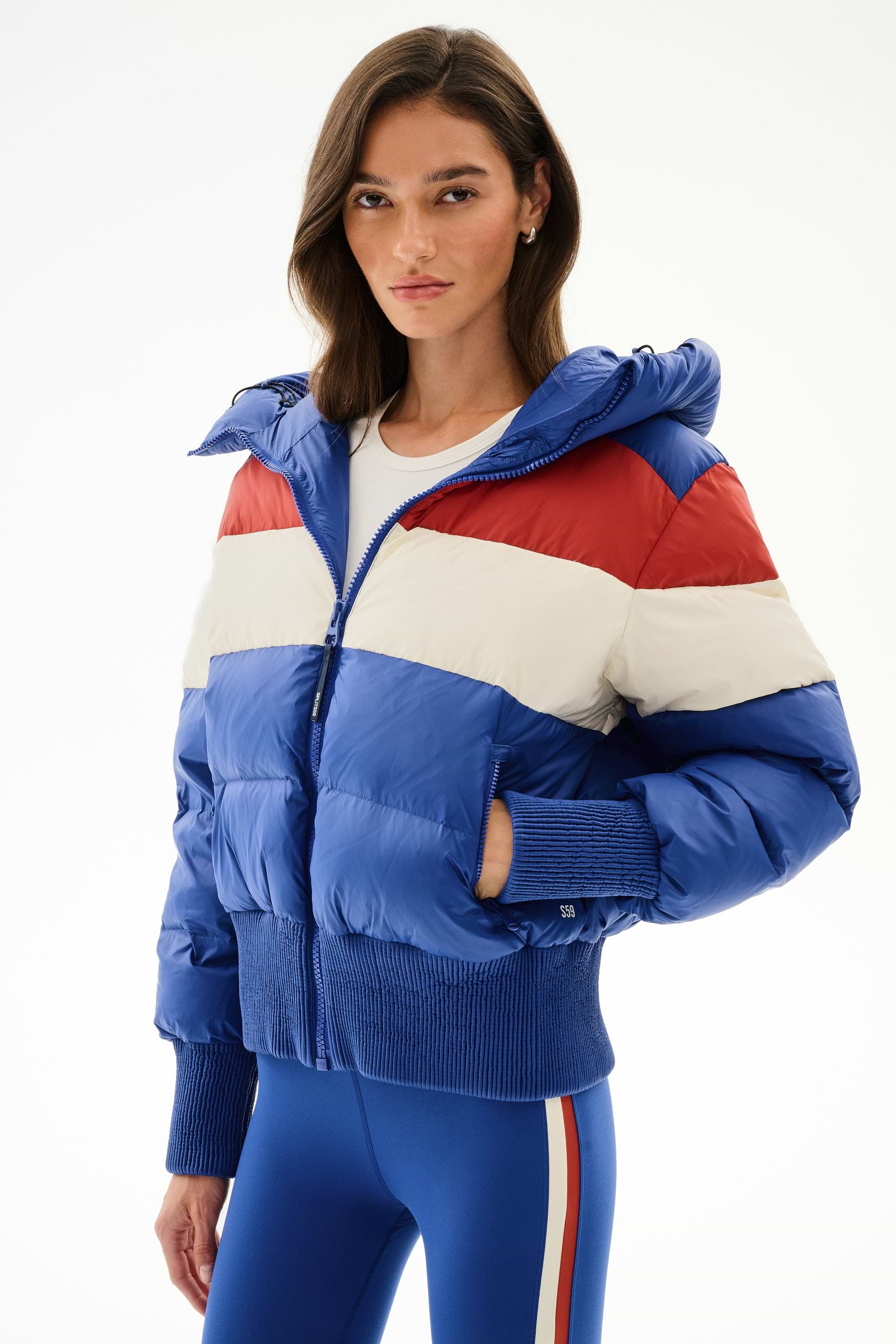 Woman wears the SPLITS59 Aspen Puffer Jacket - Cobalt/Creme with blue leggings featuring white and red side stripes.