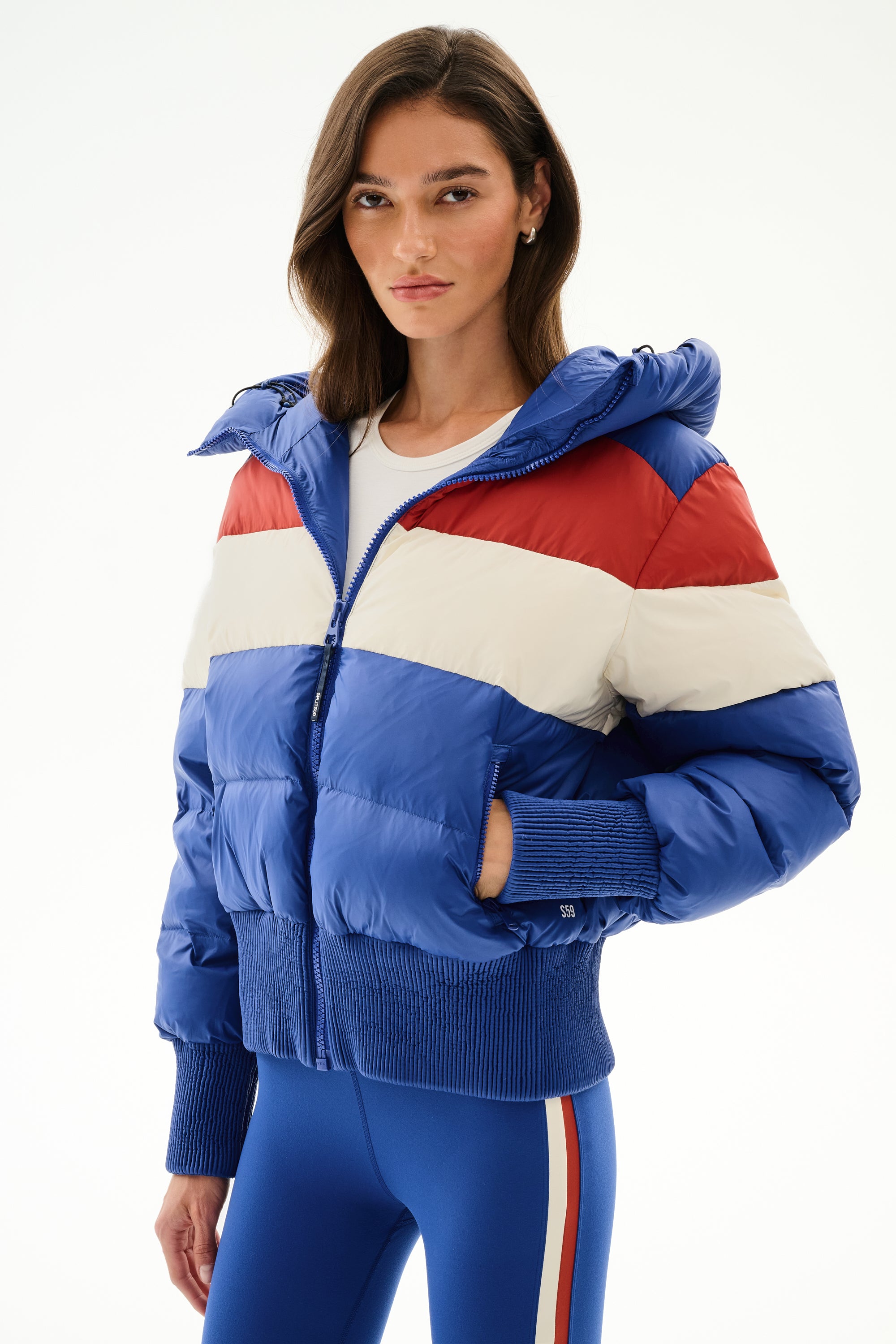Woman wears the SPLITS59 Aspen Puffer Jacket - Cobalt/Creme with blue leggings featuring white and red side stripes.
