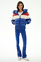 Woman faces forward wearing the SPLITS59 Aspen Puffer Jacket - Cobalt/Creme, blue flared pants with side stripes, and white sneakers.