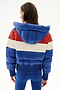 A woman faces away in the SPLITS59 Aspen Puffer Jacket - Cobalt/Creme, featuring a hood and duck down fill, paired with blue leggings against a white background.