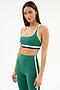A woman wears the SPLITS59 Bianca Rigor Bra in Arugula/White, featuring soft nylon-spandex fabric with white and navy trim, paired with matching high-waisted leggings, standing against a plain white background.
