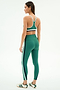 A woman, turned sideways, wears the SPLITS59 Bianca Rigor Bra in Arugula/White and matching leggings featuring white and navy stripes, paired with white sneakers with black stripes.