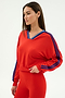 A woman wears the SPLITS59 Ellie Fleece V Neck Sweatshirt in Lotus Red/Cobalt with blue sleeve stripes and matching red spandex-blend leggings, standing against a plain light background.
