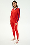 A woman wears the SPLITS59 Ellie Fleece V Neck Sweatshirt in Lotus Red/Cobalt, featuring blue sleeve stripes, paired with matching red leggings and white sneakers with red stripes.