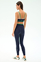 A woman faces away wearing the SPLITS59 Eva Rigor Double Strap Bra in Indigo/Spearmint, paired with matching navy leggings featuring a white side stripe and white athletic shoes with green accents.