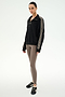 Standing against a white background, the individual is wearing the SPLITS59 Goldie French Terry Oversized Half Zip in Black/Lentil, featuring striped sleeves and soft cotton fabric, paired with taupe leggings and black Adidas sneakers.