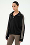 A woman wearing the SPLITS59 Goldie French Terry Oversized Half Zip in Black/Lentil, featuring soft cotton fabric and beige striped sleeves, paired with taupe leggings, stands against a plain white background.