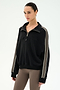 A woman wearing the SPLITS59 Goldie French Terry Oversized Half Zip in Black/Lentil, featuring soft cotton fabric and beige striped sleeves, paired with taupe leggings, stands against a plain white background.