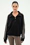 A woman wearing the SPLITS59 Goldie French Terry Oversized Half Zip in Black/Lentil, featuring striped sleeves and soft cotton fabric, paired with taupe leggings, stands against a plain white background.