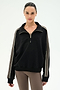A woman wearing the SPLITS59 Goldie French Terry Oversized Half Zip in Black/Lentil, featuring striped sleeves and soft cotton fabric, paired with taupe leggings, stands against a plain white background.