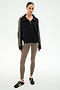 A woman stands against a plain background wearing the SPLITS59 Goldie French Terry Oversized Half Zip in Black/Lentil, featuring soft cotton fabric and striped sleeves, paired with taupe leggings and black sneakers.