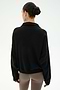 A woman with dark hair in a bun, wearing the SPLITS59 Goldie French Terry Oversized Half Zip in Black/Lentil and taupe leggings, stands facing away against a plain light background.
