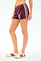 A person wears SPLITS59 Heritage Velour Short in Dark Cherry/White and white sneakers with maroon stripes, standing against a plain white background.