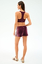 A woman stands facing away, wearing the SPLITS59 Heritage Velour Short in Dark Cherry/White, paired with a burgundy sports bra and sneakers.