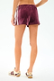 A person stands with their back to the camera, wearing SPLITS59 Heritage Velour Short in Dark Cherry/White and cream sneakers featuring maroon accents.