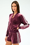 A woman poses with one hand on her waist, wearing the SPLITS59 Heritage Velour Bomber in Dark Cherry/White, paired with matching shorts featuring white side stripes, set against a plain background.