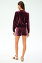 A person stands facing away, wearing the SPLITS59 Heritage Velour Bomber in Dark Cherry/White with matching shorts, made from soft polyester-spandex, paired with beige sneakers featuring maroon stripes against a plain light background.