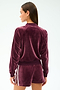 A woman stands with her back to the camera, wearing the SPLITS59 Heritage Velour Bomber in Dark Cherry/White, featuring white sleeve stripes and shorts, made from a soft polyester-spandex blend for comfort and flexibility.