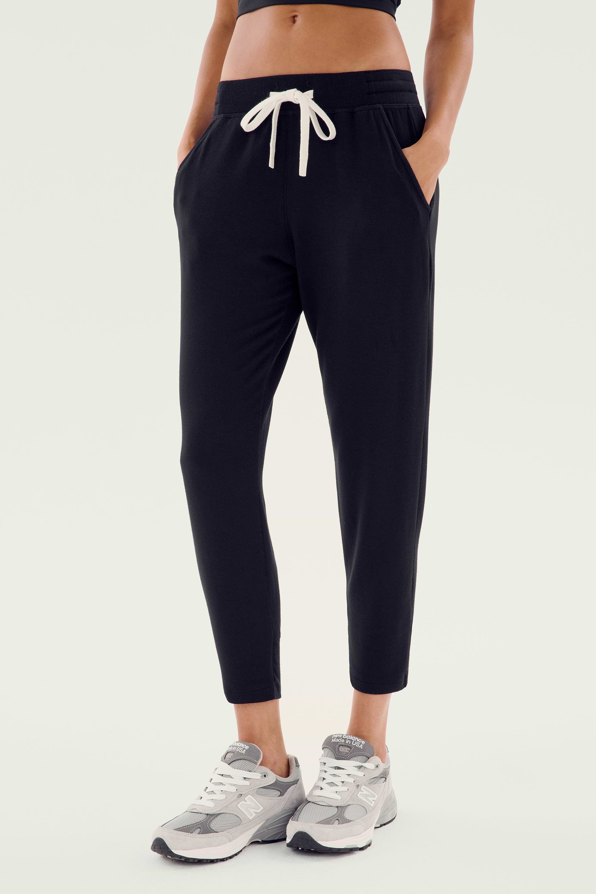 A person wearing the Reena Fleece 7/8 Sweatpant in Black by Splits59, paired with gray sneakers, epitomizes comfort and style.